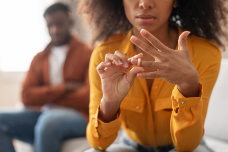 Woman taking off wedding ring with husband behind her